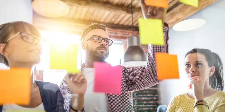 A close up of three people working with post it notes organizing thoughts