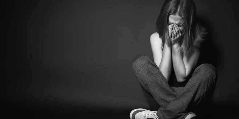 A black and white image of a woman resting on the floor holding her face in distress