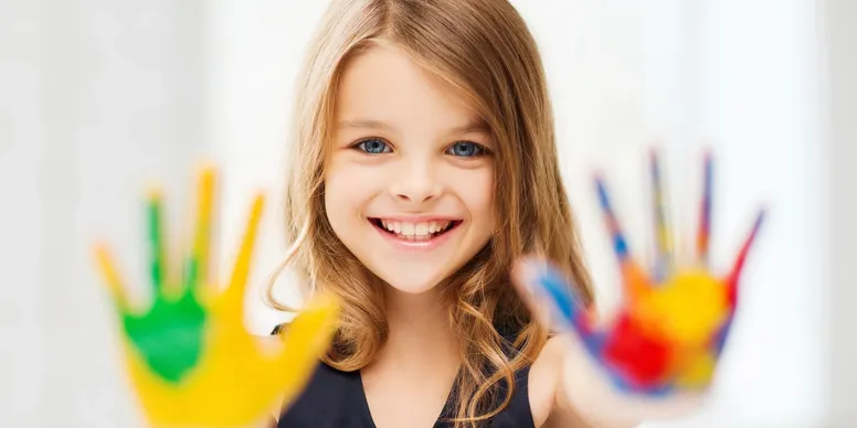 A young girl holding her hands up covered in paint while smiling