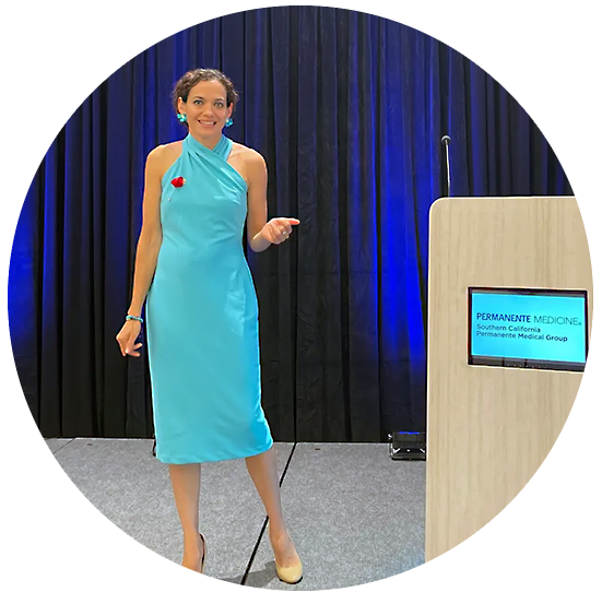 Dr. Diana on stage speaking beside a podium with a blue curtain in the background