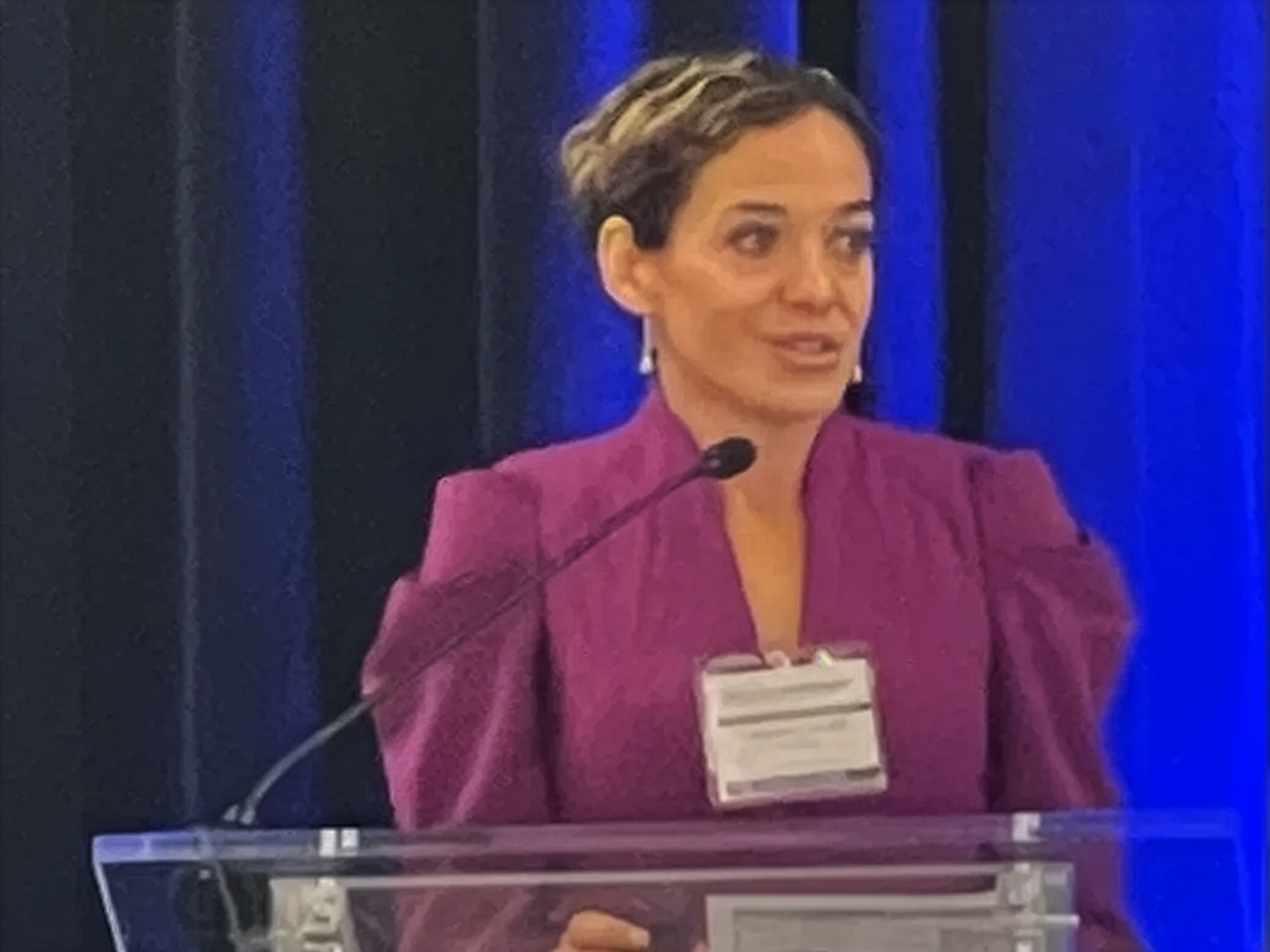 Dr Diana standing at a podium speaking in front of a blue curtain