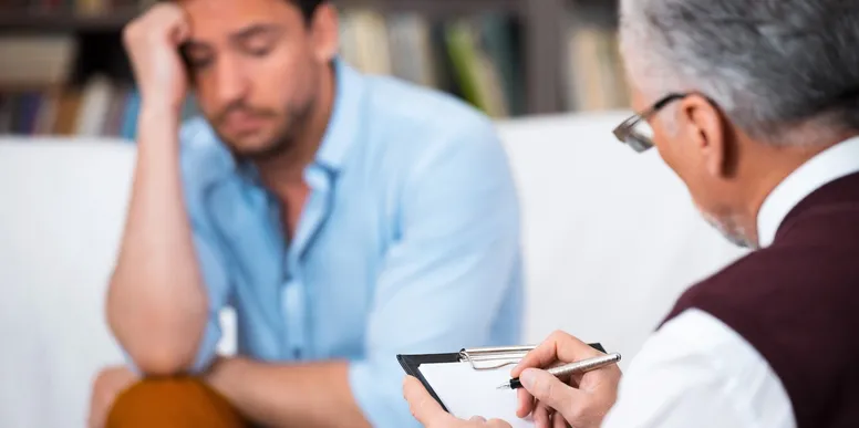 A doctor taking notes seated in front of a patient on the couch