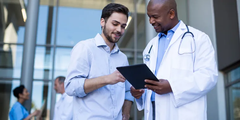 A doctor smiling showing a patient a chart standing outside a building