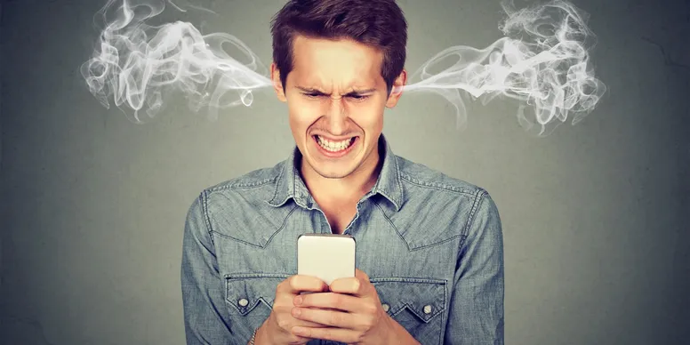 A man looking agrily at his phone in his hands with smoke pouring out of his ears from anger