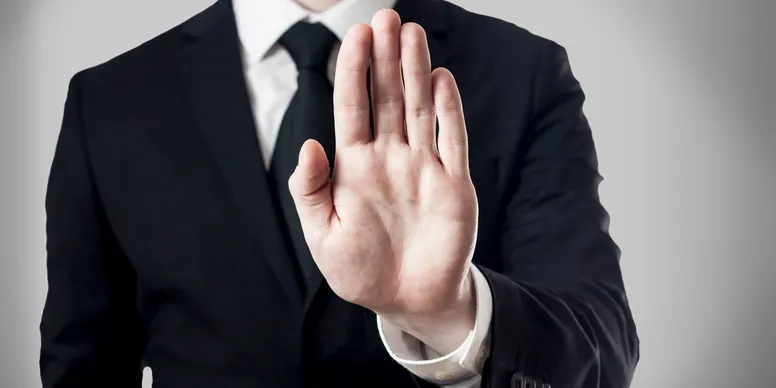 A man in a suit holding his had up facing forward in a stop motion